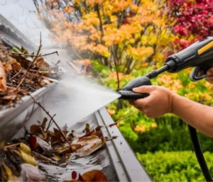 Close-up of a clogged gutter being pressure cleaned to remove leaves, twigs, and debris, preventing water overflow and gutter damage.