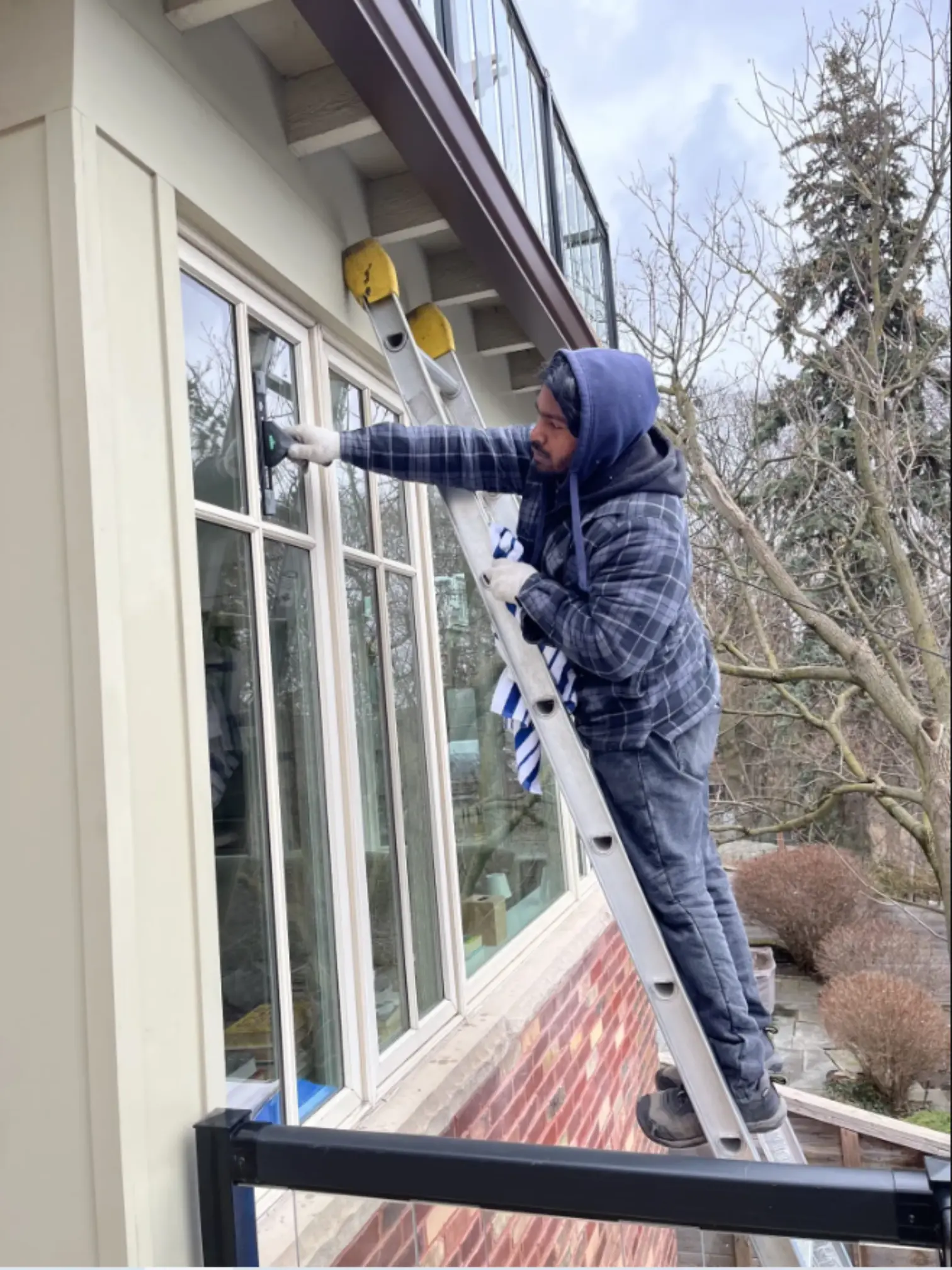Professional worker cleaning residential windows on ladder during window cleaning service in Toronto, Ontario