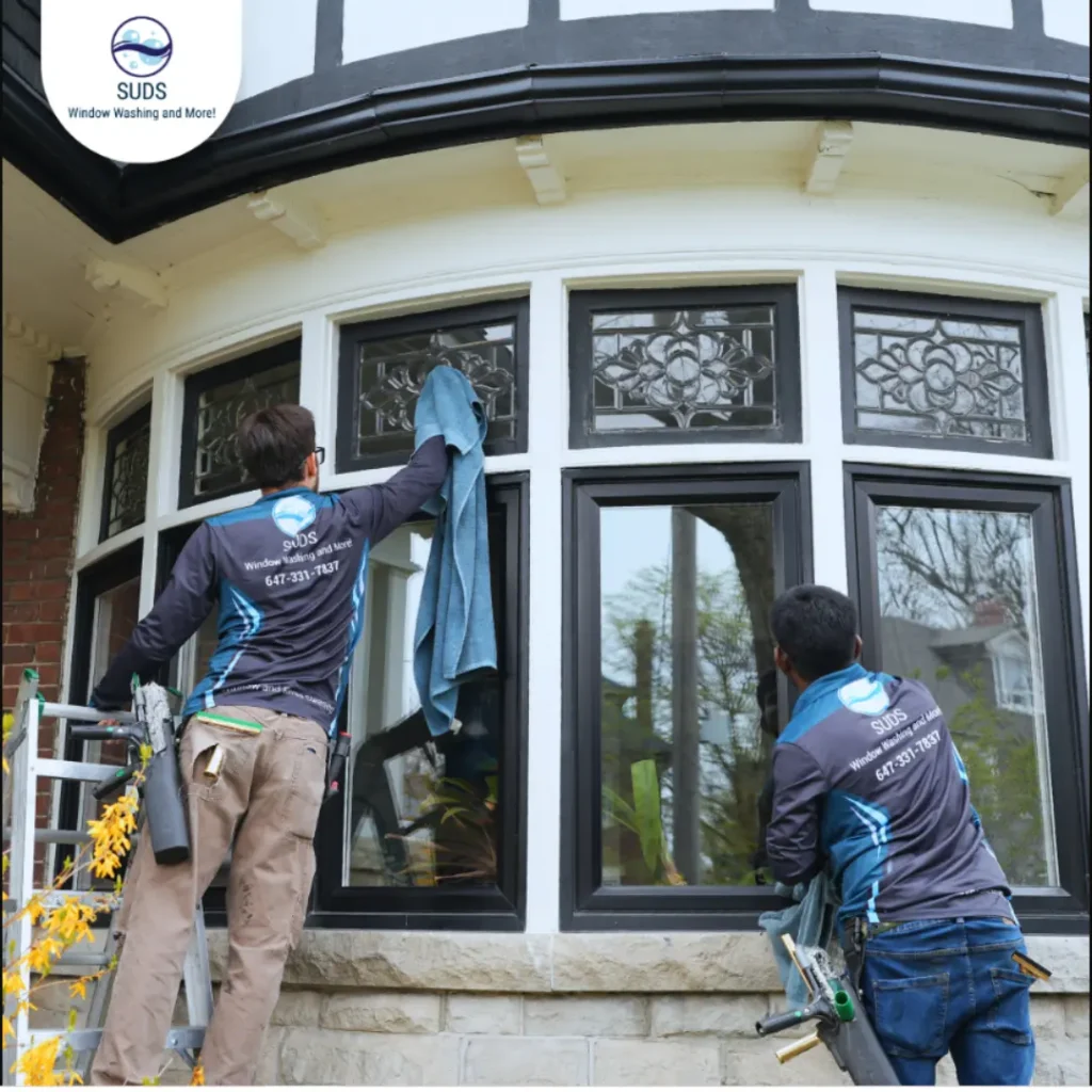 Professional technicians from SUDS Window and Eaves Cleaning washing complex exterior residential bay windows in Toronto, illustrating the pros of professional window cleaning vs DIY.