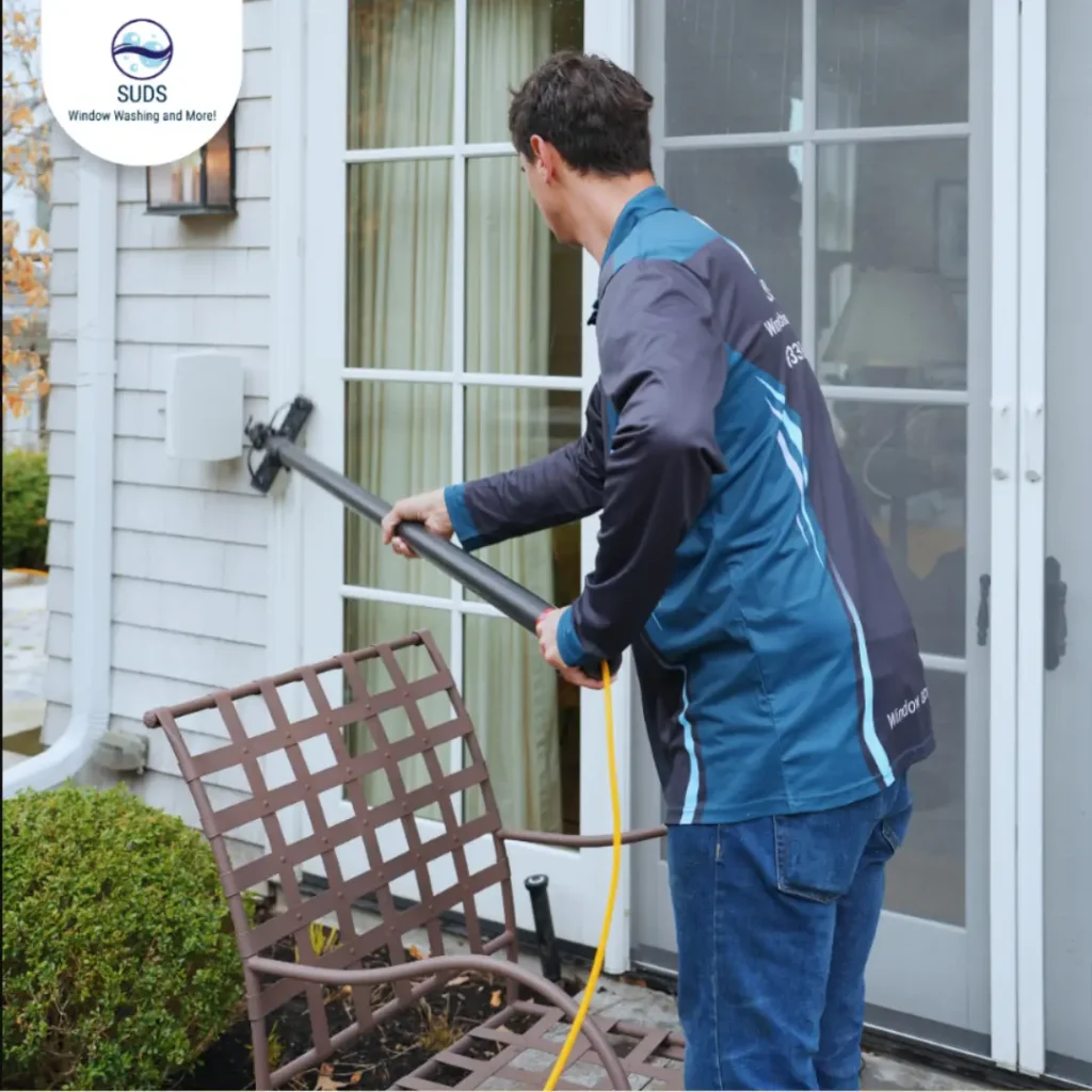 SUDS Window and Eaves Cleaning technician using a water-fed pole system to tackle tough hard water stains on residential patio door glass in Toronto.