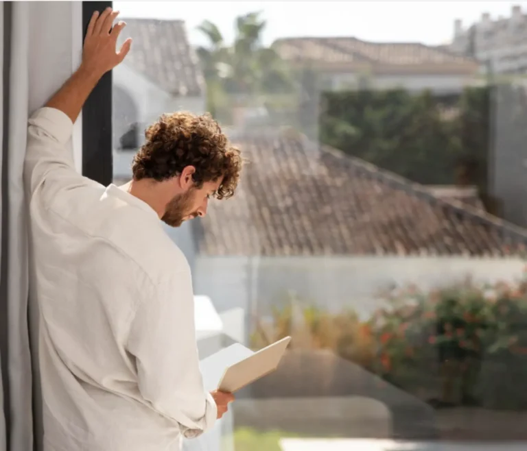 Person reading beside a large clean window with abundant natural sunlight, demonstrating how clear windows can improve mood, focus, and productivity.