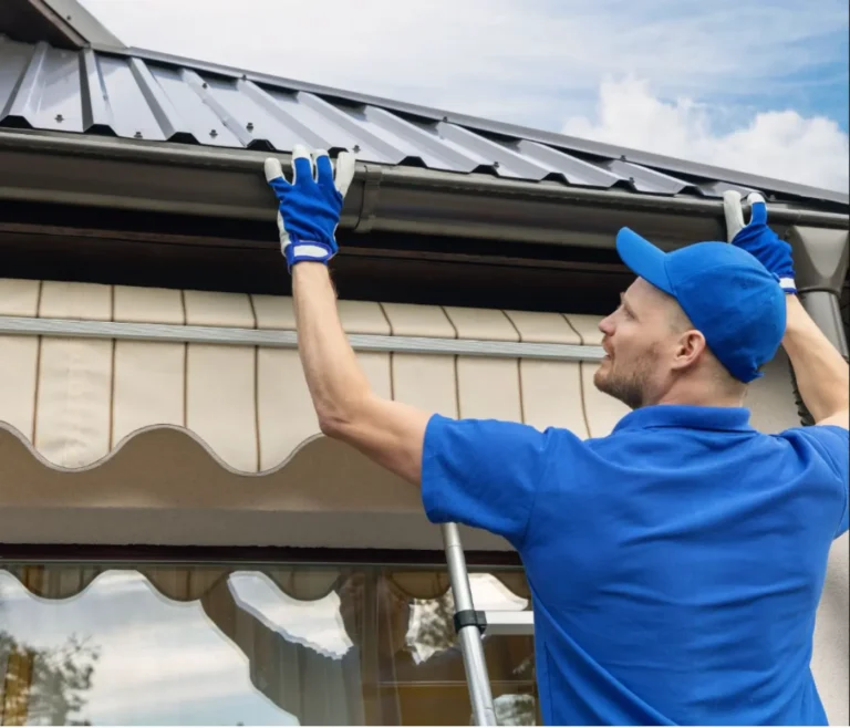 A professional technician wearing heavy-duty gloves and a blue uniform inspecting a residential eavestrough system to prevent gutter cleaning repair costs.